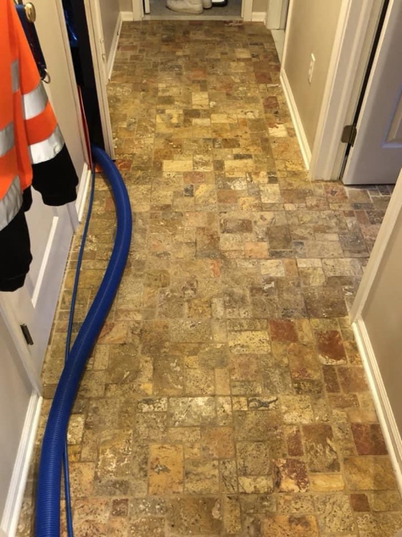 A travertine tile floor being cleaned with a blue hose